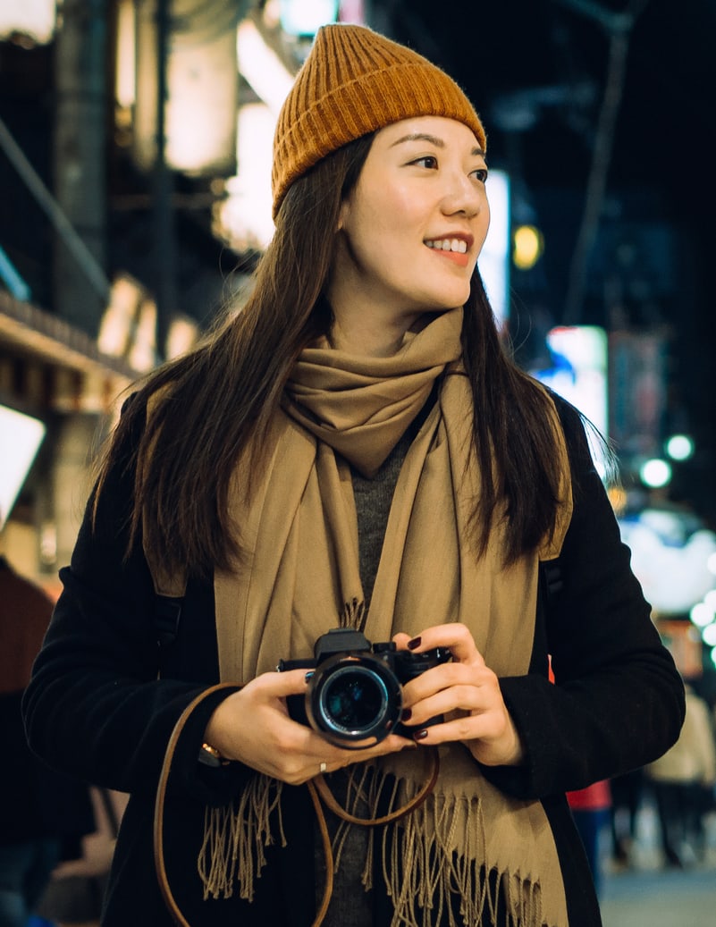 A young woman wearing a hat is holding a camera at night